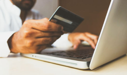 Person holding credit card in hand about to make a purchase in their laptop