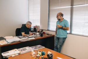 Person seated on office chair engaged in discussion with person standing across office desk