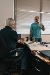 Person seated on office chair engaged in discussion with person standing across office desk
