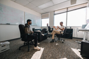 People seated on office chairs in the middle of an office engaged in conversation