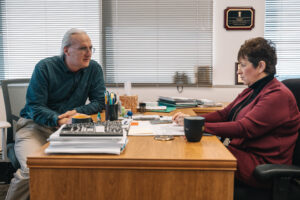 Person seated on office chair engaged in discussion with person seated across office desk